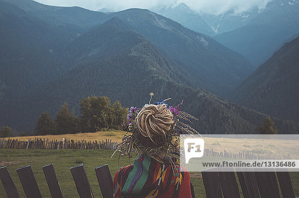 Rückansicht einer Frau mit Dreadlocks Haarknoten  die auf einem Feld vor Bergen steht