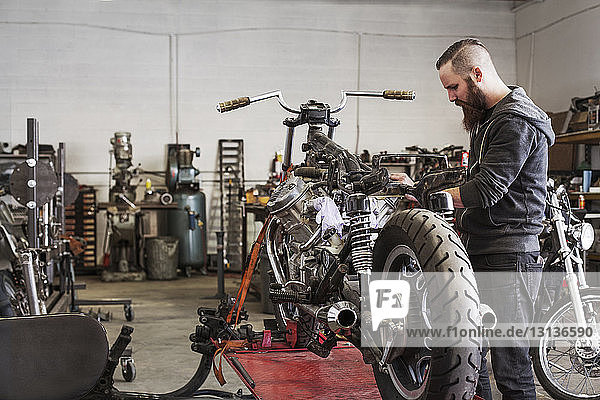 Seriöser Mechaniker  der in einer Reparaturwerkstatt am Motorrad arbeitet