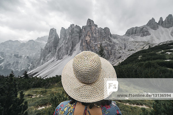 Rear view of female hiker wearing hat standing on mountain against cloudy sky