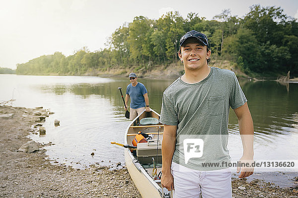 Porträt eines jungen Mannes  der mit einem Freund ein Boot in Richtung Seeufer schiebt