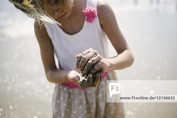 Mädchen spielt mit Sand  während sie am Strand am Ufer steht