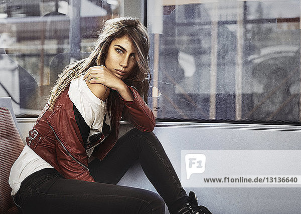 Porträt einer selbstbewussten jungen Frau in Lederjacke in Seitenansicht  die im Bus sitzt