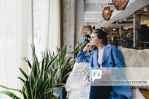 Young woman holding smart phone while looking through window at cafe