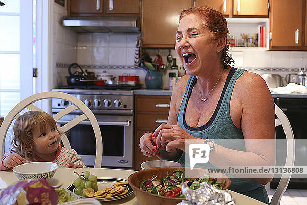 Fröhliche Großmutter bereitet das Essen zu  während sie mit der Enkelin am Tisch sitzt