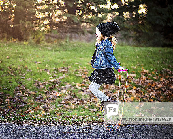 Side view of girl jumping rope on footpath at park during autumn