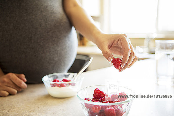Cropped image of pregnant woman holding raspberry at table