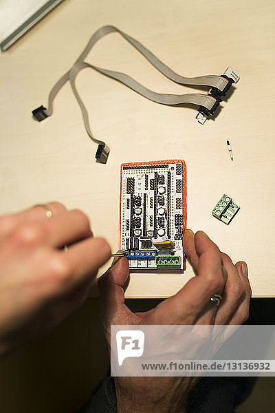 Cropped hands of engineer repairing mother board on table in office