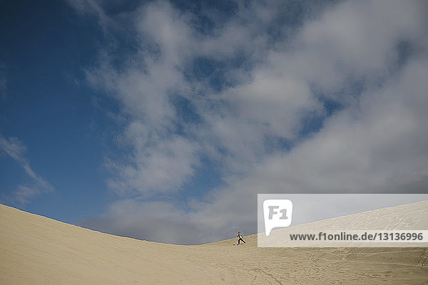Distant view of boy running on sand against blue sky