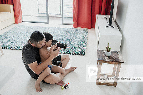 Hochwinkelaufnahme von Vater und Sohn beim Fotografieren zu Hause auf dem Boden sitzend