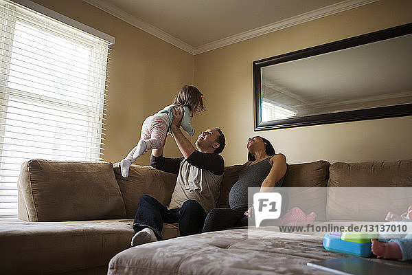 Eltern spielen mit der Tochter  während sie zu Hause auf dem Sofa sitzen