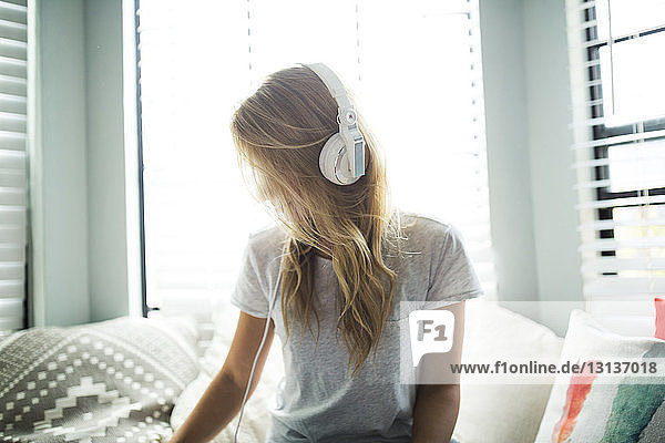 Frau hört Musik über Kopfhörer  während sie auf einem Fensterplatz in einer Nische sitzt