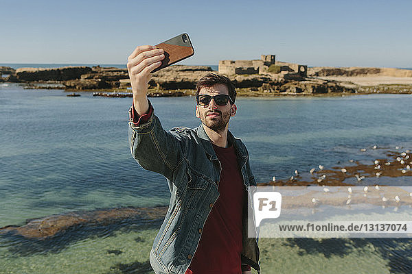 Man taking selfie while standing at beach against clear sky