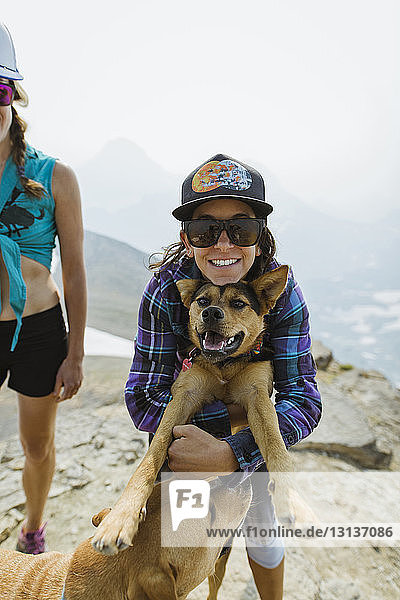 Porträt einer Frau  die einen Hund umarmt  während sie bei einem Freund auf einem Berg vor klarem Himmel steht