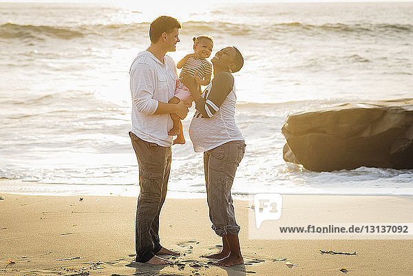 Glückliche Eltern spielen mit ihrer Tochter  während sie am Strand stehen