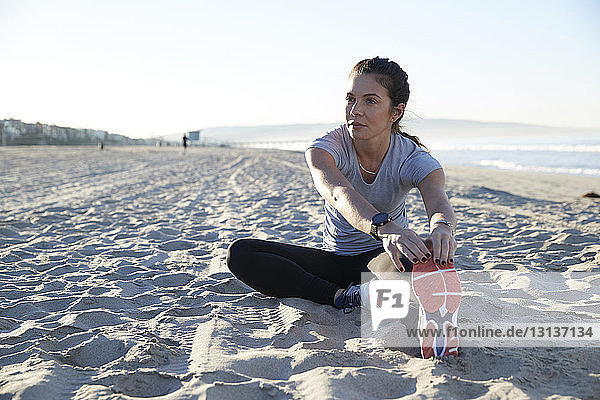 Zuversichtliche Frau  die ihr Bein beim Sport am Strand streckt