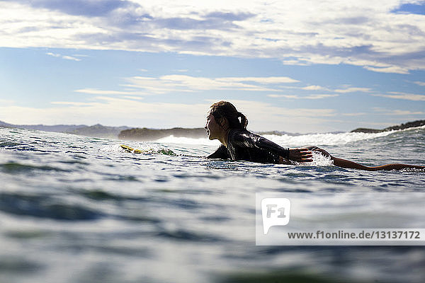 Seitenansicht einer Surferin  die auf einem Surfbrett im Meer liegt