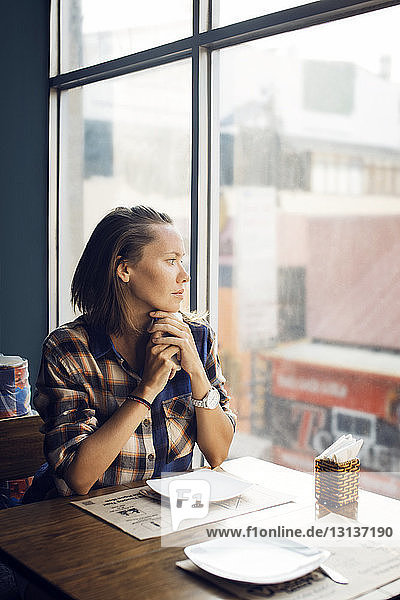 Nachdenkliche Frau  die durch das Fenster schaut  während sie im Café sitzt
