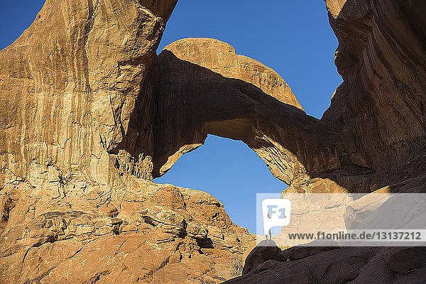 Frau in voller Länge steht auf einer Felsformation im Arches-Nationalpark vor klarem  blauem Himmel