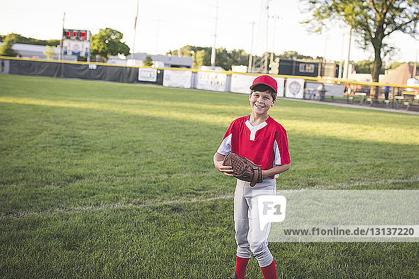 Porträt eines lächelnden Baseball-Spielers in Uniform auf grasbewachsenem Spielfeld stehend
