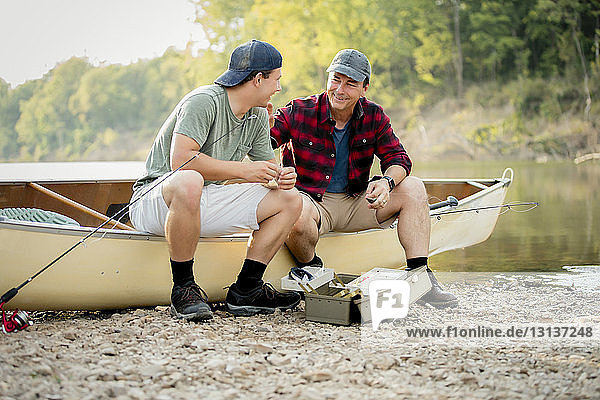 Happy friends talking while adjusting fishing tackles on boat at lakeshore