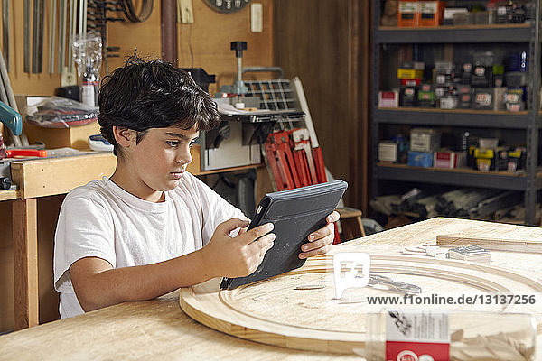 Boy using tablet computer while sitting in workshop