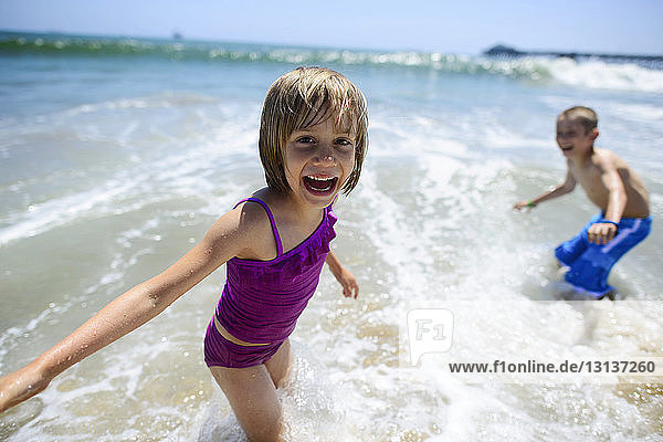 Porträt eines glücklichen Mädchens  das mit seinem Bruder im Meer am Strand von Oceanside spielt