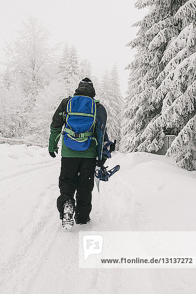 Rear view of man with snowboard walking on snow covered field
