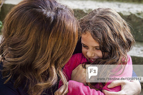 Nahaufnahme einer glücklichen Mutter  die ihre Tochter kitzelt  während sie im Freien sitzt