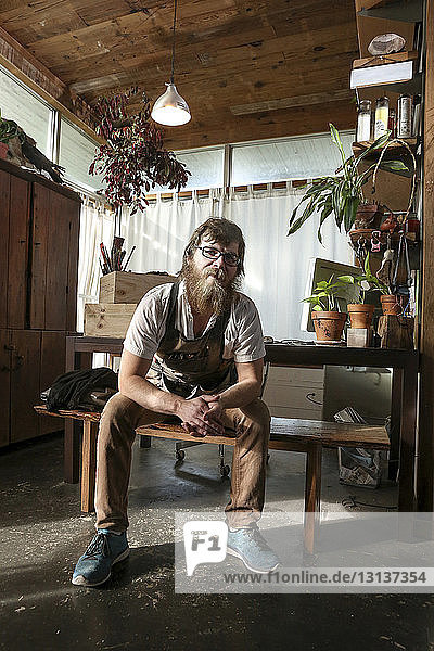 Porträt eines selbstbewussten Tischlers  der in der Werkstatt auf einer Bank sitzt