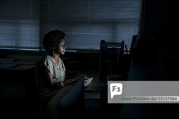 Seitenansicht einer Geschäftsfrau  die am Desktop-Computer arbeitet  während sie im Büro am Schreibtisch sitzt