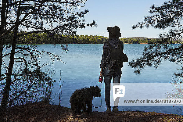 Rear view of woman with dog standing by lake against clear sky