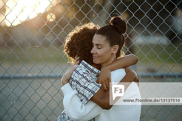 Loving mother and son embracing against chainlink fence at basketball court