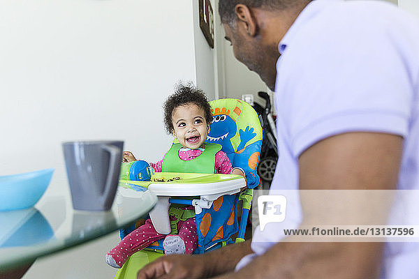 Happy daughter looking at father while sitting on high chair