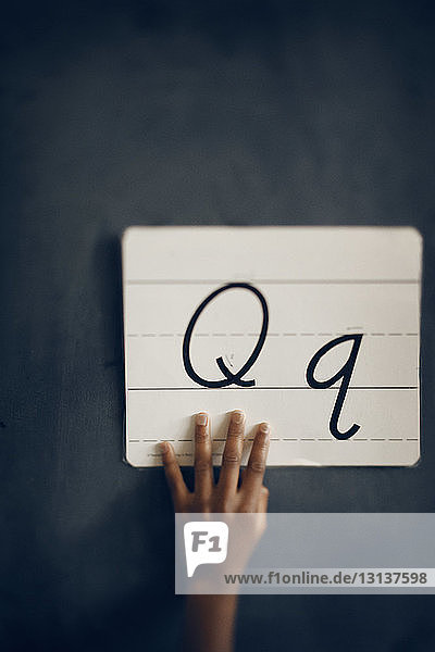 Nahaufnahme eines handhaltenden Papiers mit Q-Alphabeten an der Tafel