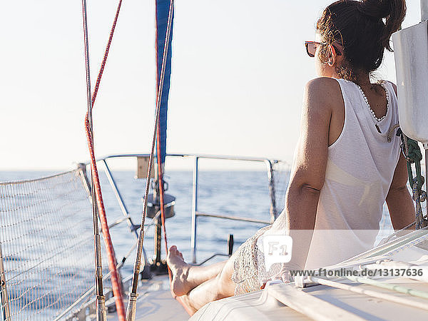 Rückansicht einer mittelgroßen erwachsenen Frau  die im Segelboot sitzend bei klarem Himmel auf das Meer blickt