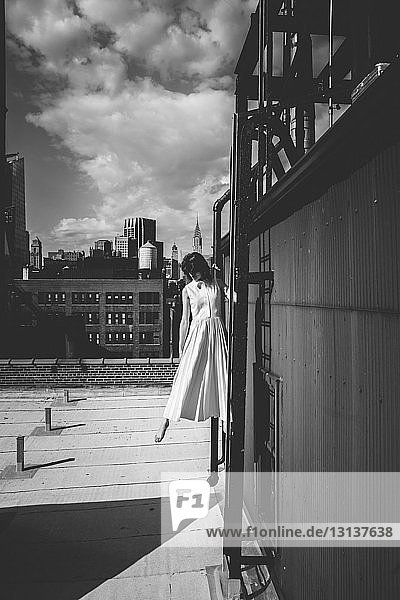 Frau steht auf der Leiter einer Gebäudeterrasse gegen den Himmel in der Stadt