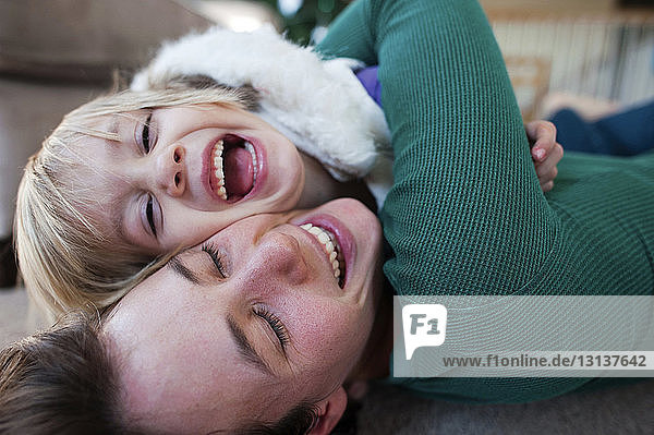 Glückliche Mutter umarmt Tochter  während sie zu Hause auf dem Teppich liegt