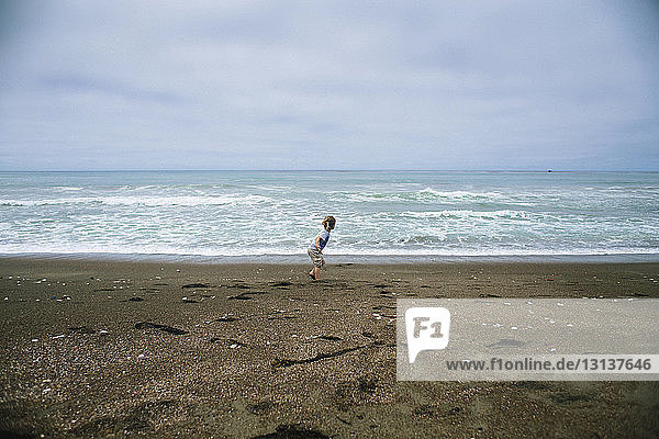 Mädchen rennt auf Sand am Strand gegen bewölkten Himmel