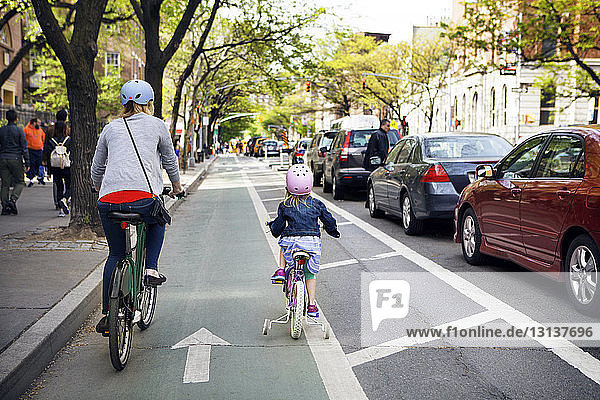 Rückansicht von Mutter und Tochter beim Fahrradfahren in der Stadt