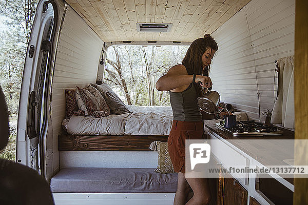 Side view of woman making drink while standing in motor home