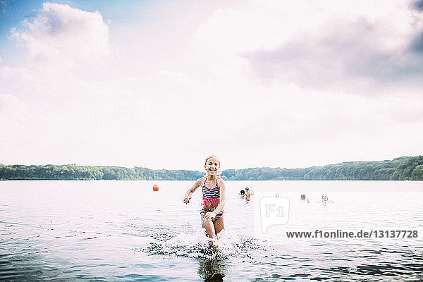 Cheerful girl running in lake against cloudy sky