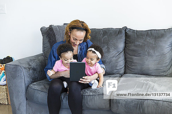 Mutter und Töchter schauen auf Tablet-Computer  während sie auf dem Sofa sitzen
