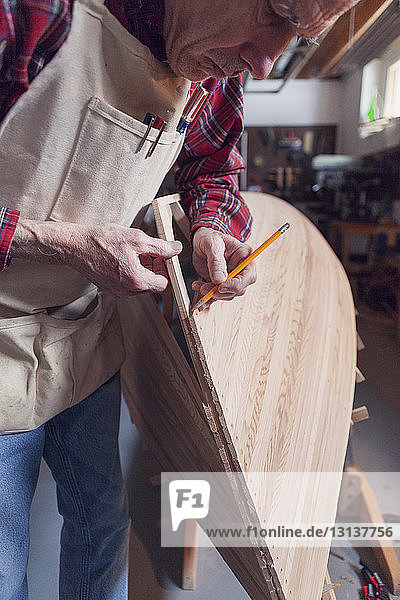 Älterer Mann mit Bleistift auf Holzboot im Workshop