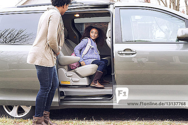 Woman looking at daughter while standing by car