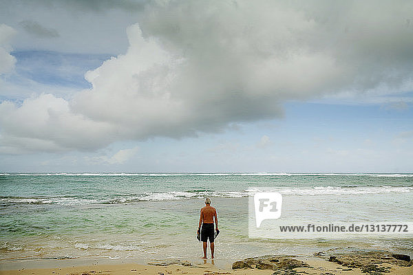 Rear view of man standing on seashore against cloudy sky