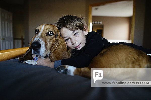 Porträt eines Jungen  der einen Hund umarmt  während er auf dem Bett liegt