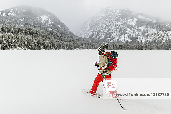 Seitenansicht einer Frau mit Rucksack beim Wandern in schneebedeckter Landschaft