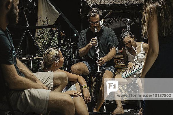 Mann und Frau spielen Musikinstrumente  während sie mit Freunden am Ferienort sitzen