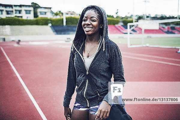 Happy female athlete in hooded jacket standing on running tracks