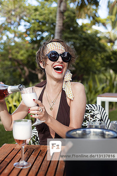 Fröhliche Frau schenkt Champagner in Glas bei Tisch ein